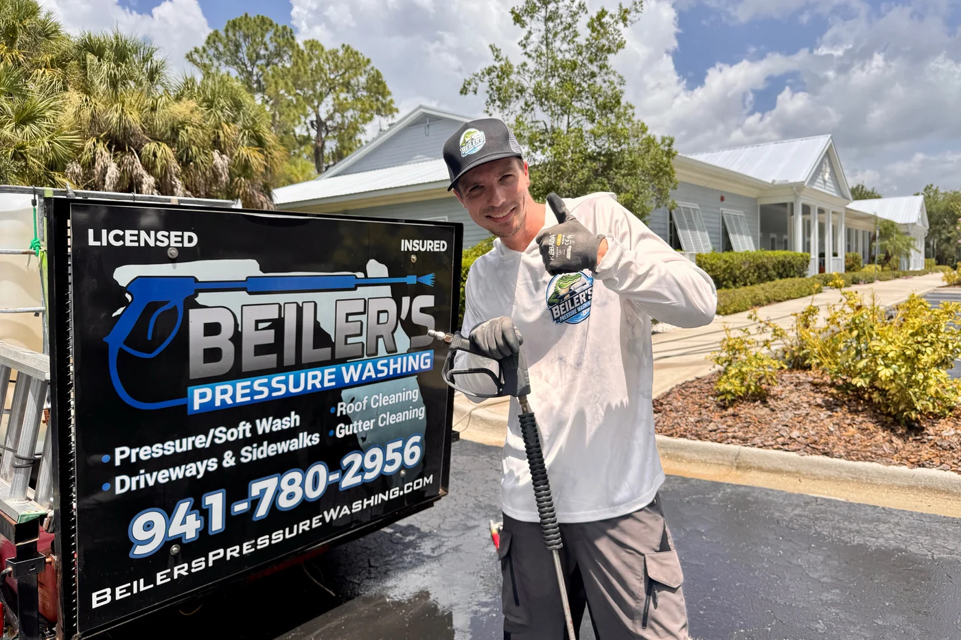 David Beiler, owner of Beiler's Pressure Washing, holding a pressure washing wand beside his branded trailer at a Sarasota job site
